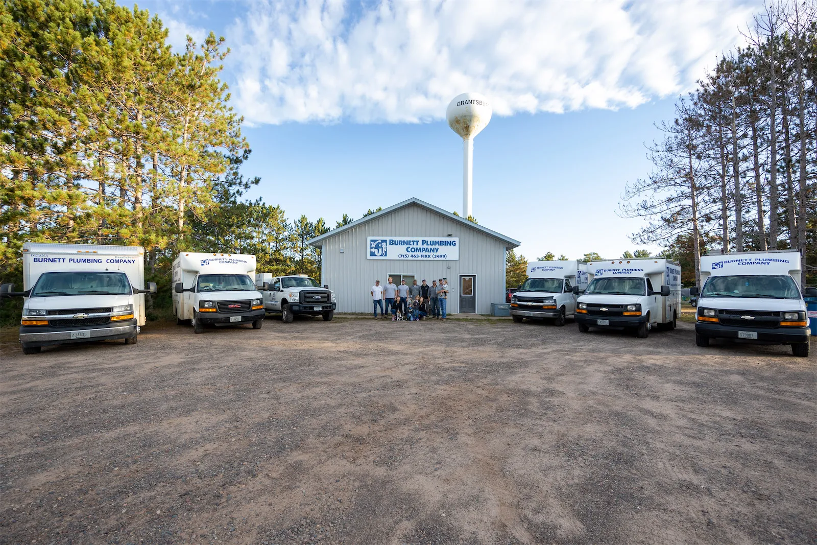 A group photo of the employees and vehicles of Burnett Plumbing Company.