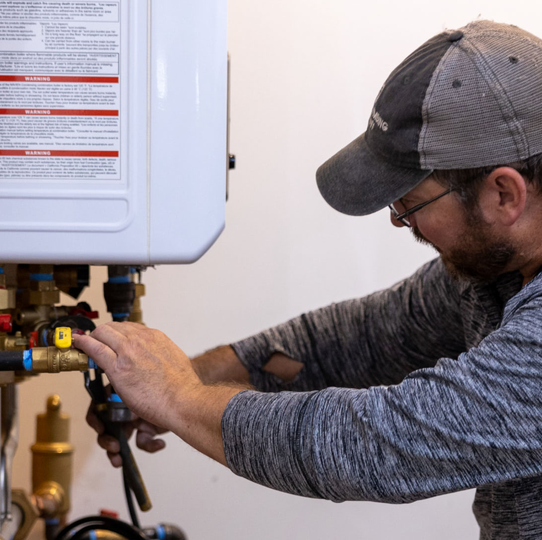 A man working on plumbing for a hot water heater.